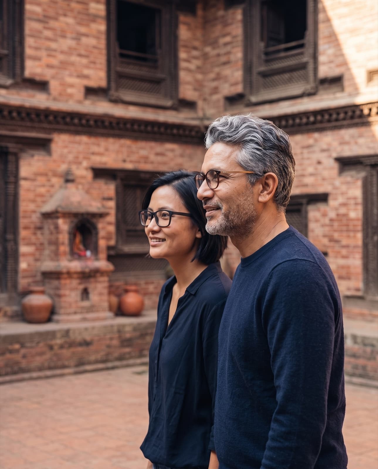Two people in glasses walking through a Patan brick courtyard