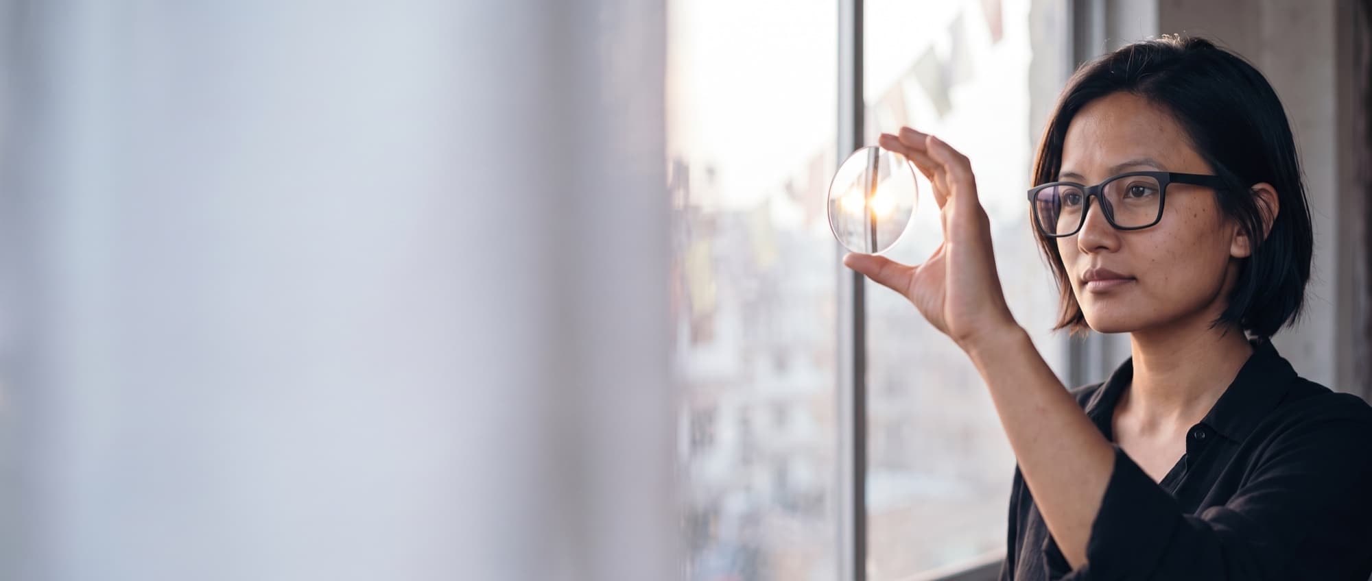 A woman at a café window holding a clear lens up to the daylight