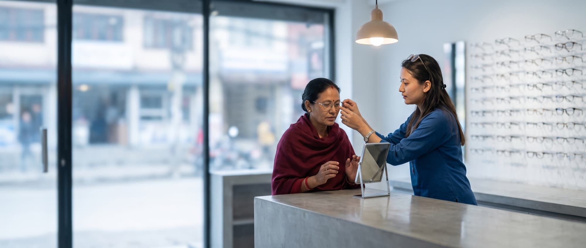 An optician helping a customer try frames at a partner store counter